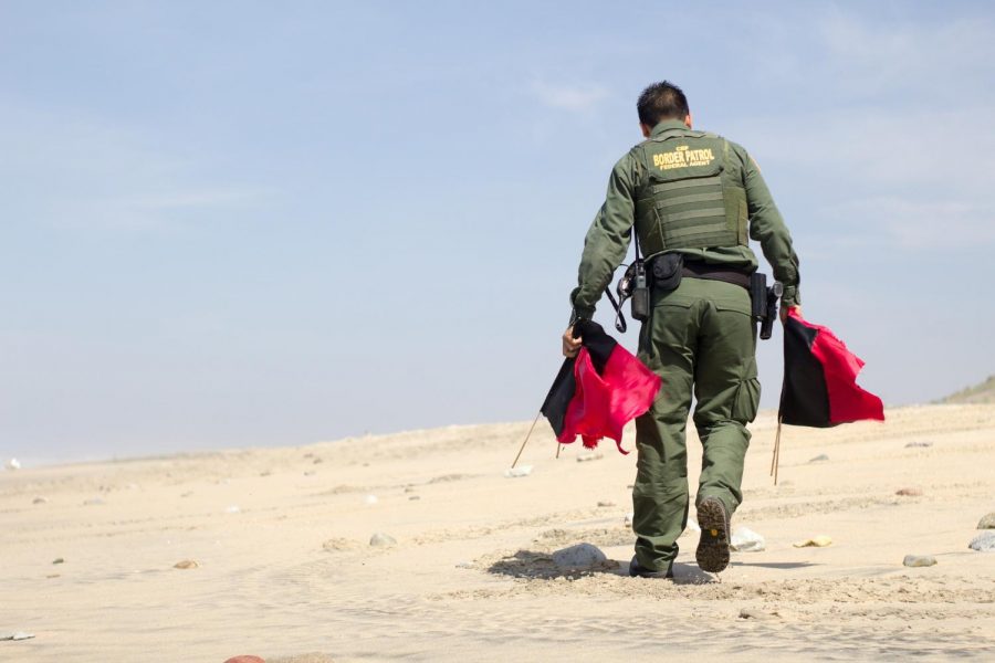 A US border patrol agent marking the border in a barren desert with red flags.