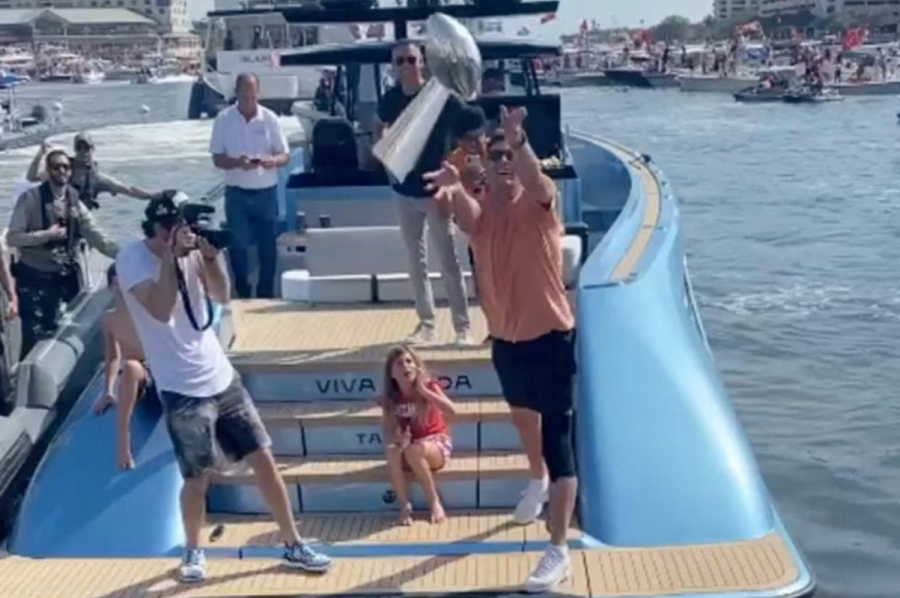 Brady celebrates superbowl victory by throwing the Superbowl trophy to the neighboring boat.
